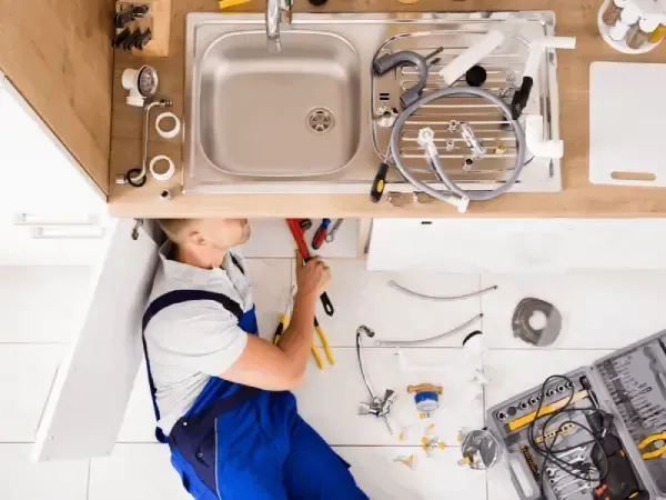 A plumber is fixing a sink in a kitchen.
