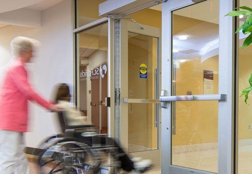 Person pushing a wheelchair through glass double doors with automatic door operators