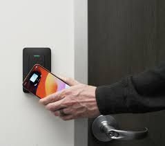 Hand holding a smartphone near a wall-mounted smart lock to unlock a door