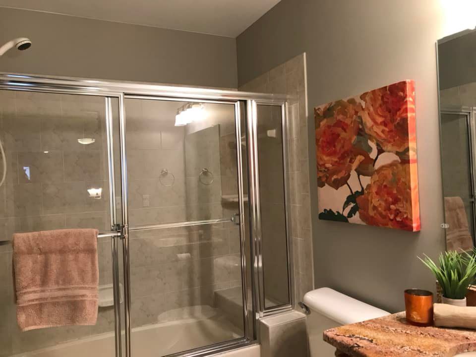 A bathroom with a shower , toilet , sink and a painting on the wall.