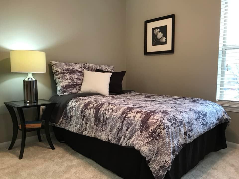 A bedroom with a bed , nightstand , lamp and picture on the wall.