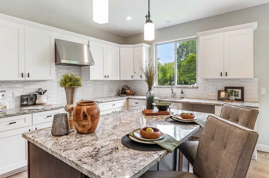 A kitchen with granite counter tops , white cabinets , and a large island.