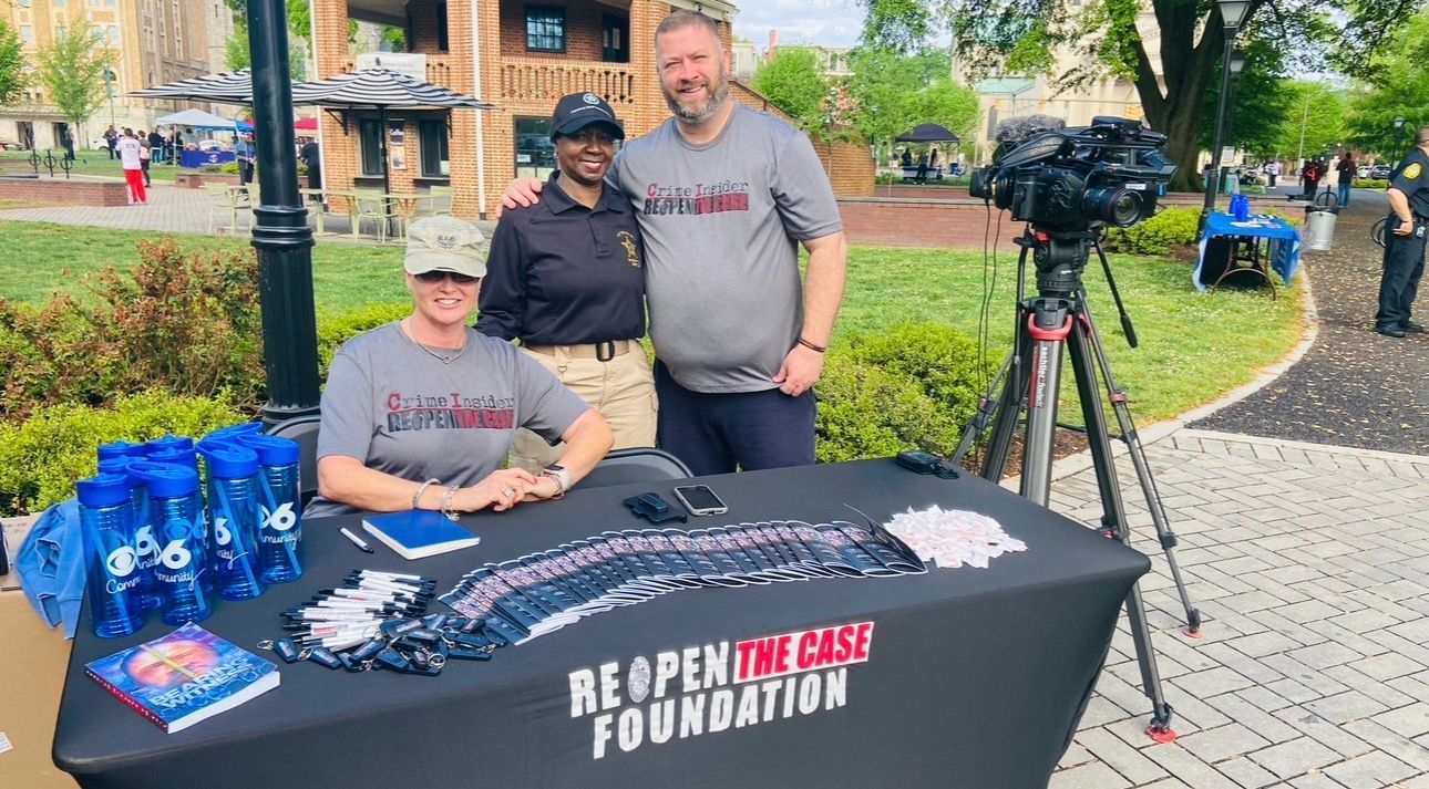 People gather in a bright community room, talking and standing among rows of chairs during an informal indoor event.