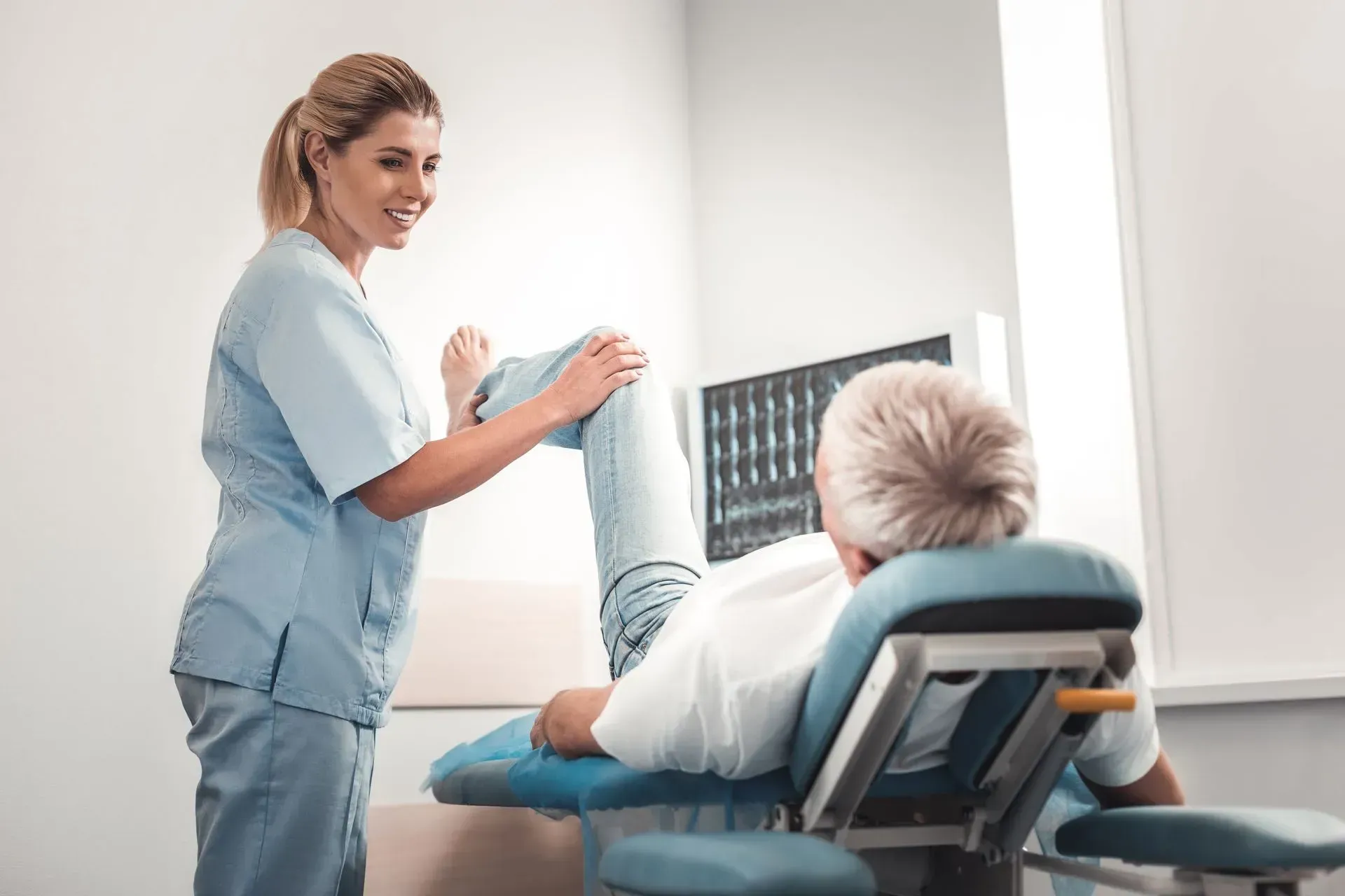 Physical therapist stretches a patient's leg in a medical office, focusing on knee movement.