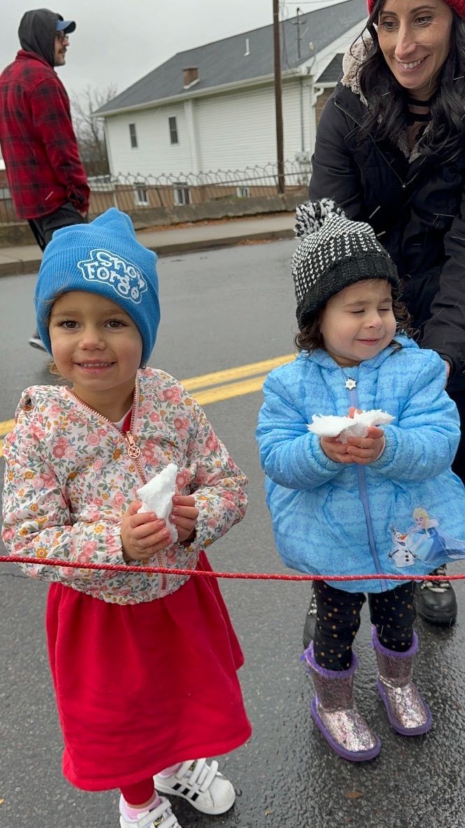 Two children in hats and coats holding snow, standing outside, smiling.