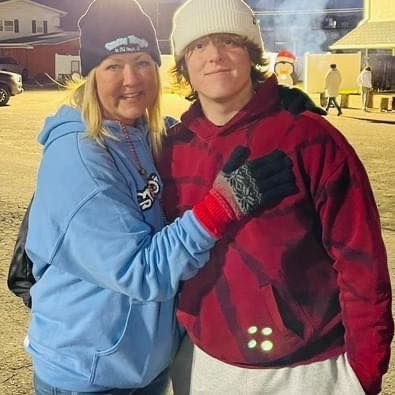 Woman in blue sweatshirt and teen in red hoodie pose together outside at night.