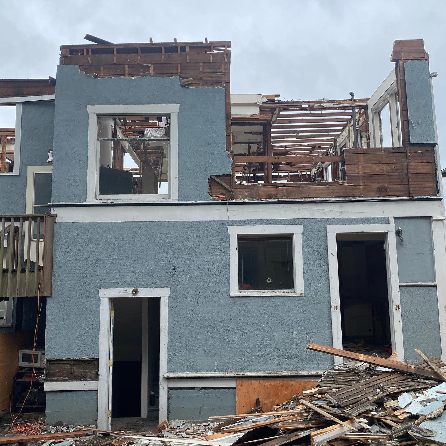 A blue house is being demolished with a pile of wood in front of it