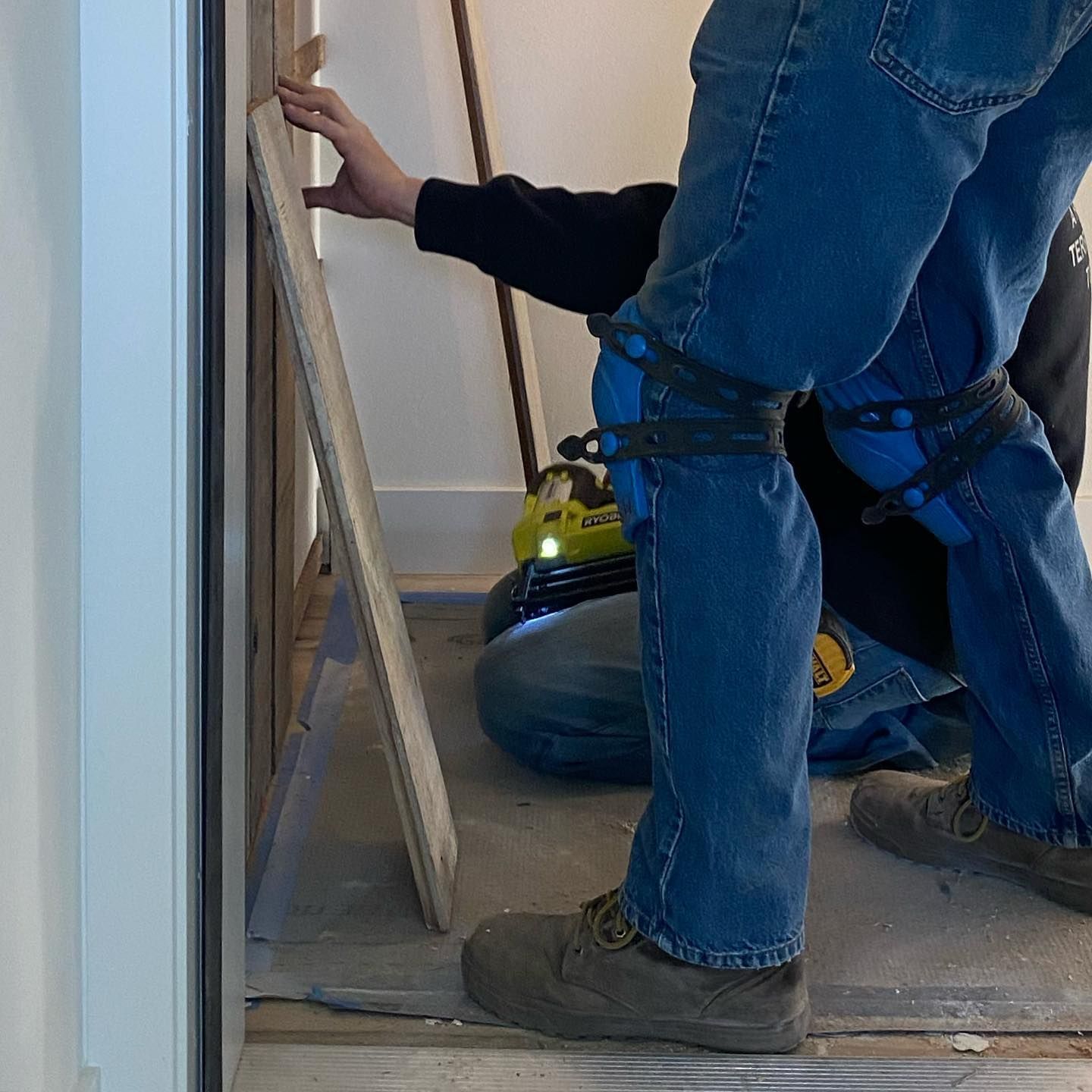 A man is kneeling on the floor holding a piece of wood.