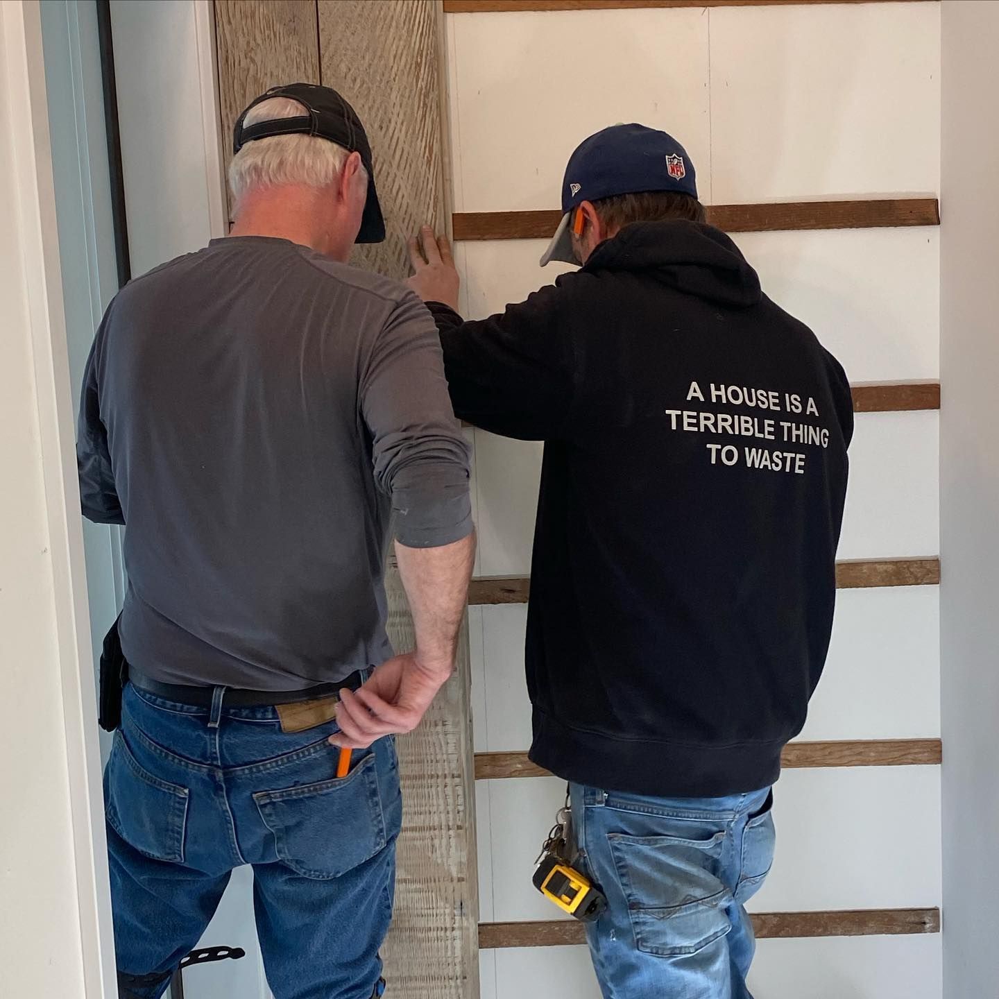 Two men standing next to each other with one wearing a shirt that says a house is a terrible thing to waste