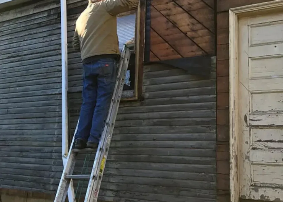 A man is standing on a ladder on the side of a building.