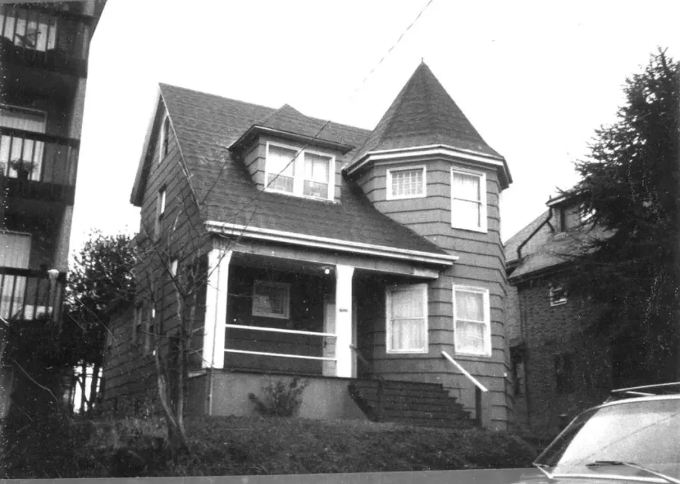 A black and white photo of a house with a car parked in front of it