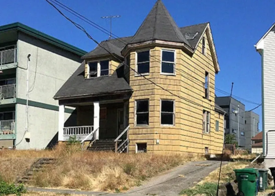 A yellow house with a gray roof is sitting on top of a grassy hill.