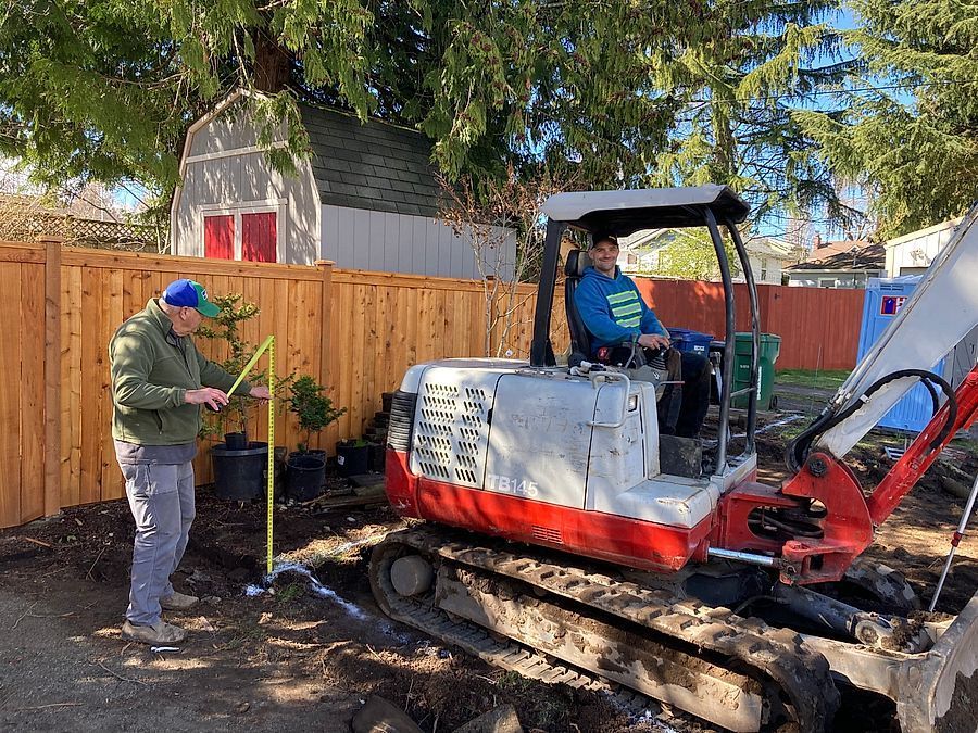 A man is measuring a hole in the ground next to a bulldozer.