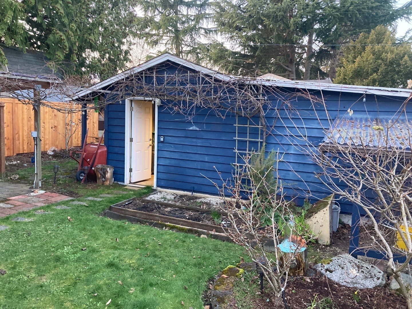 A blue shed with a white door is in the backyard of a house.