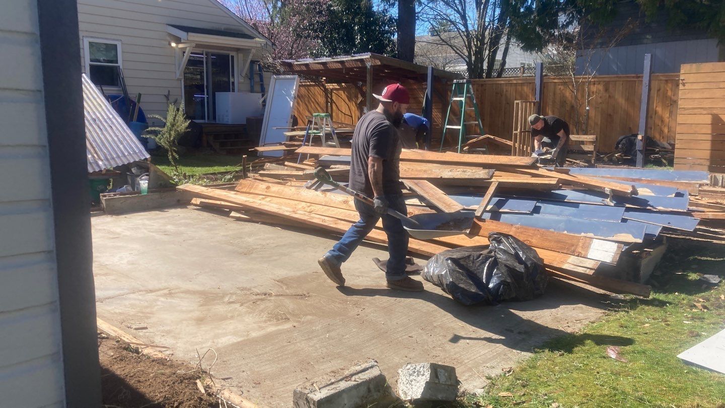 A man is walking down a sidewalk next to a pile of wood.
