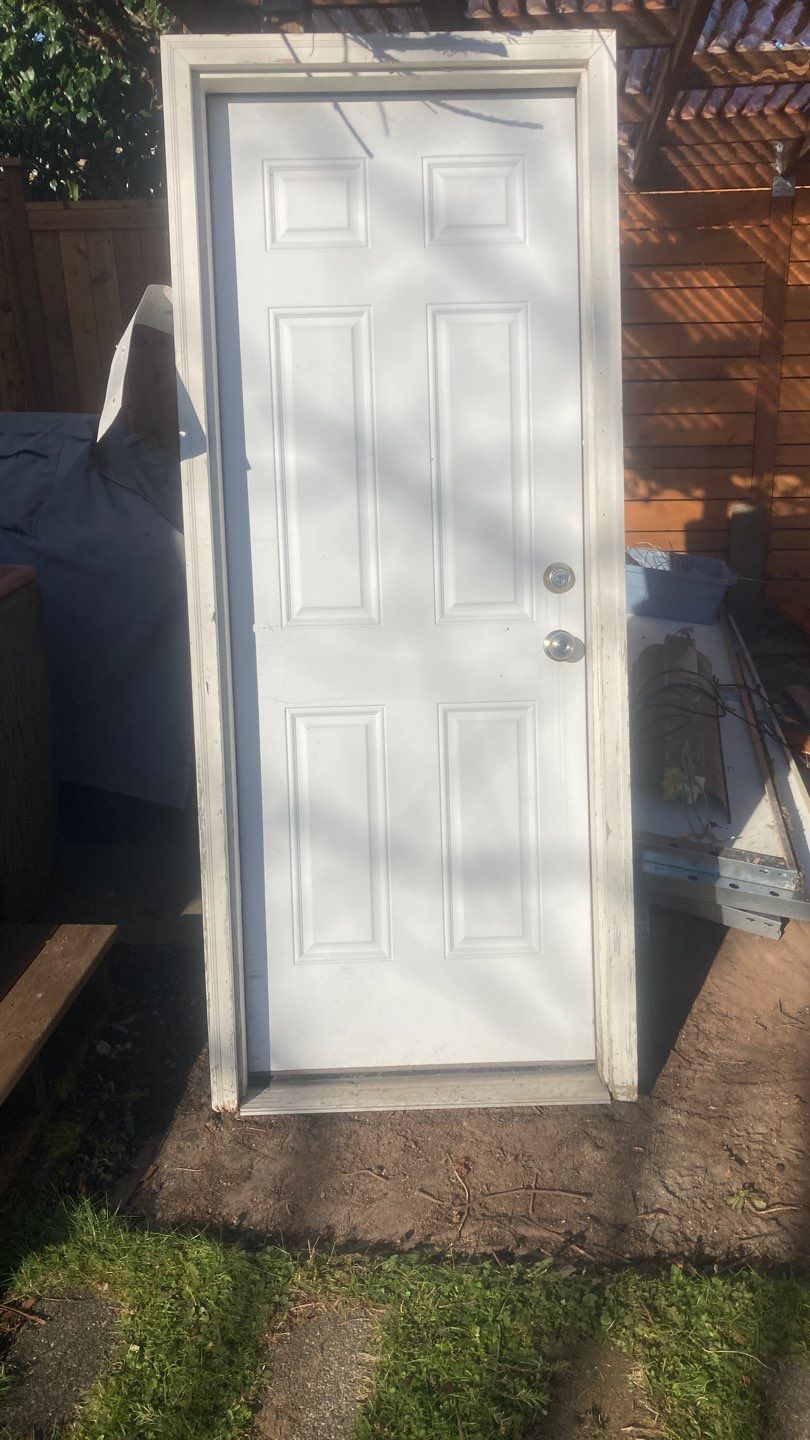 A white door is sitting on top of a concrete floor in a yard.
