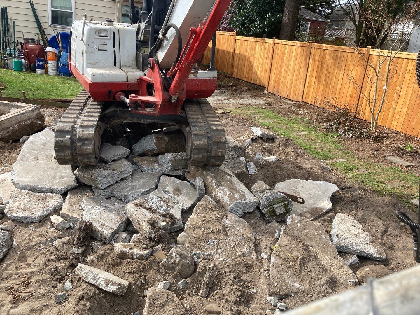 A red and white excavator is sitting on top of a pile of rocks in a backyard.