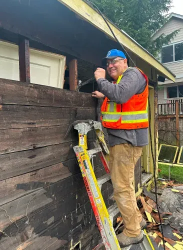 A man is standing on a ladder next to a wooden building.