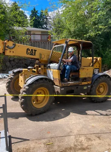 A man is driving a yellow cat forklift on a construction site.