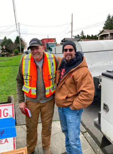 Two men are standing next to each other on a sidewalk in front of a truck.