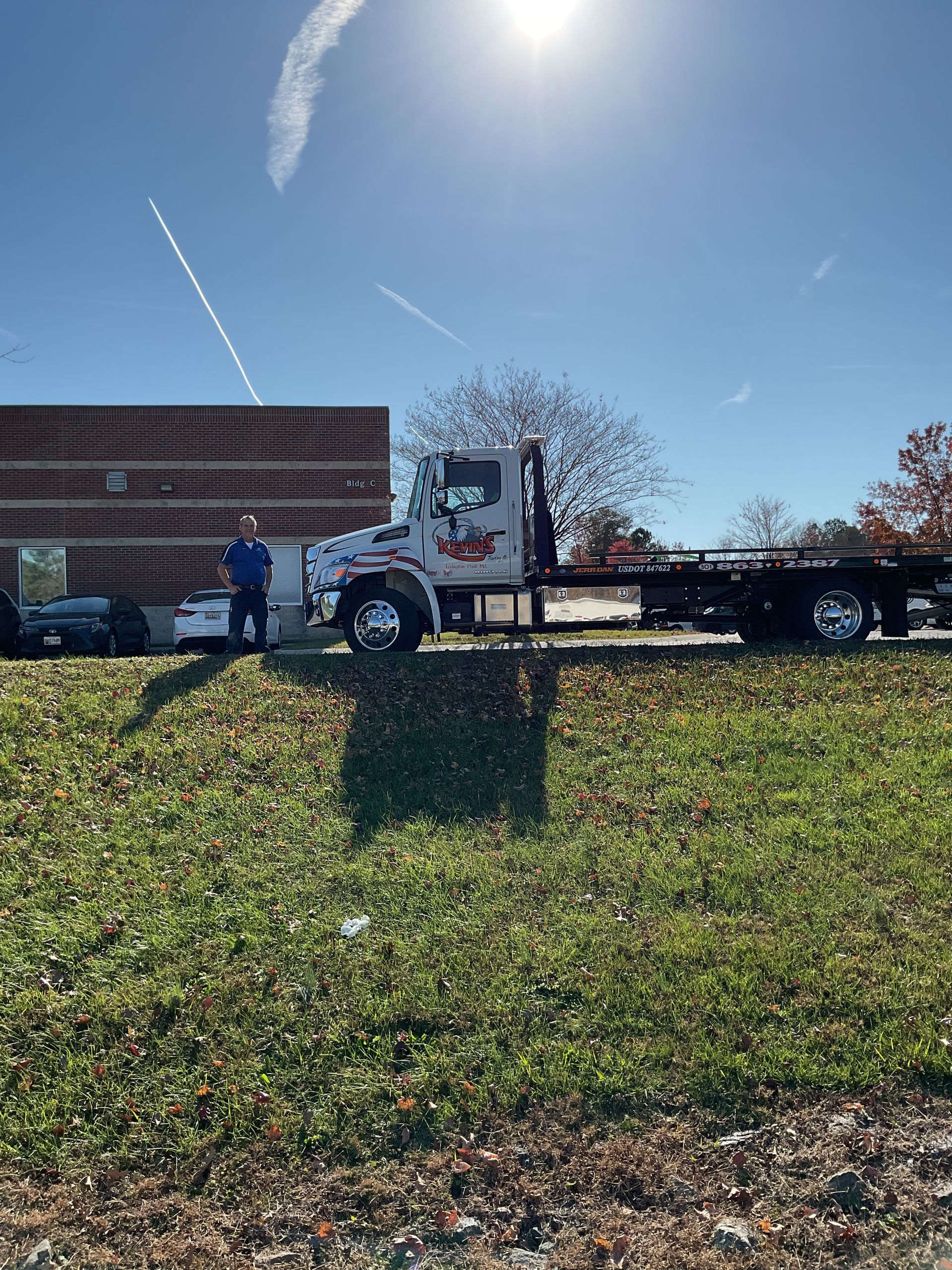 Tow truck parked roadside with a person nearby on a sunny day.