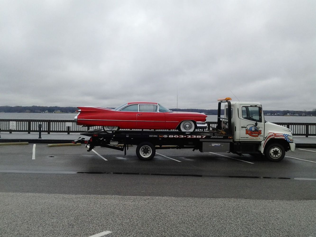 Red vintage car being towed on a flatbed tow truck on a bridge