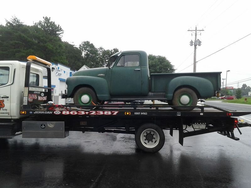 Green vintage pickup truck being towed on a flatbed tow truck