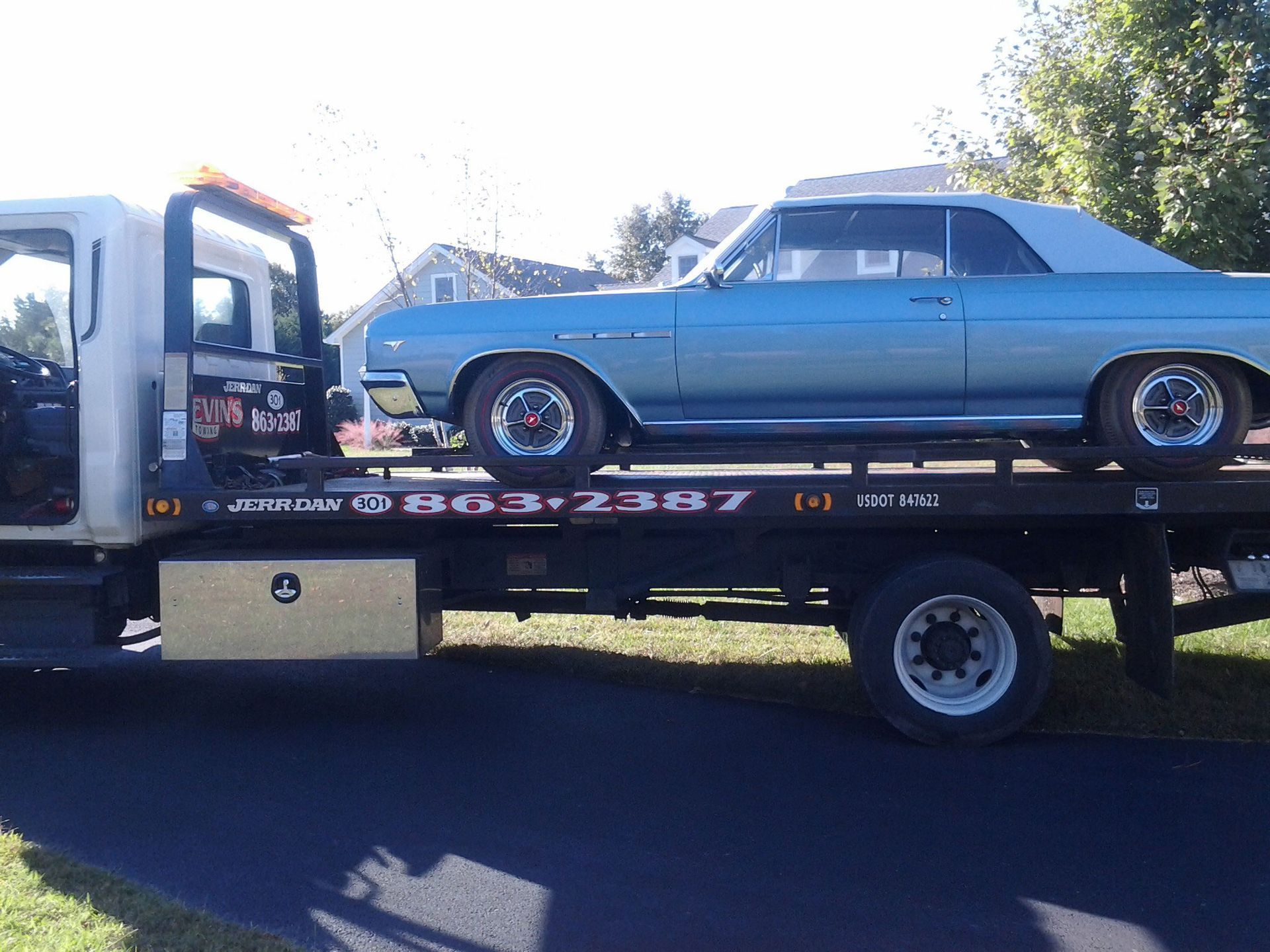 A light blue vintage convertible on a flatbed tow truck