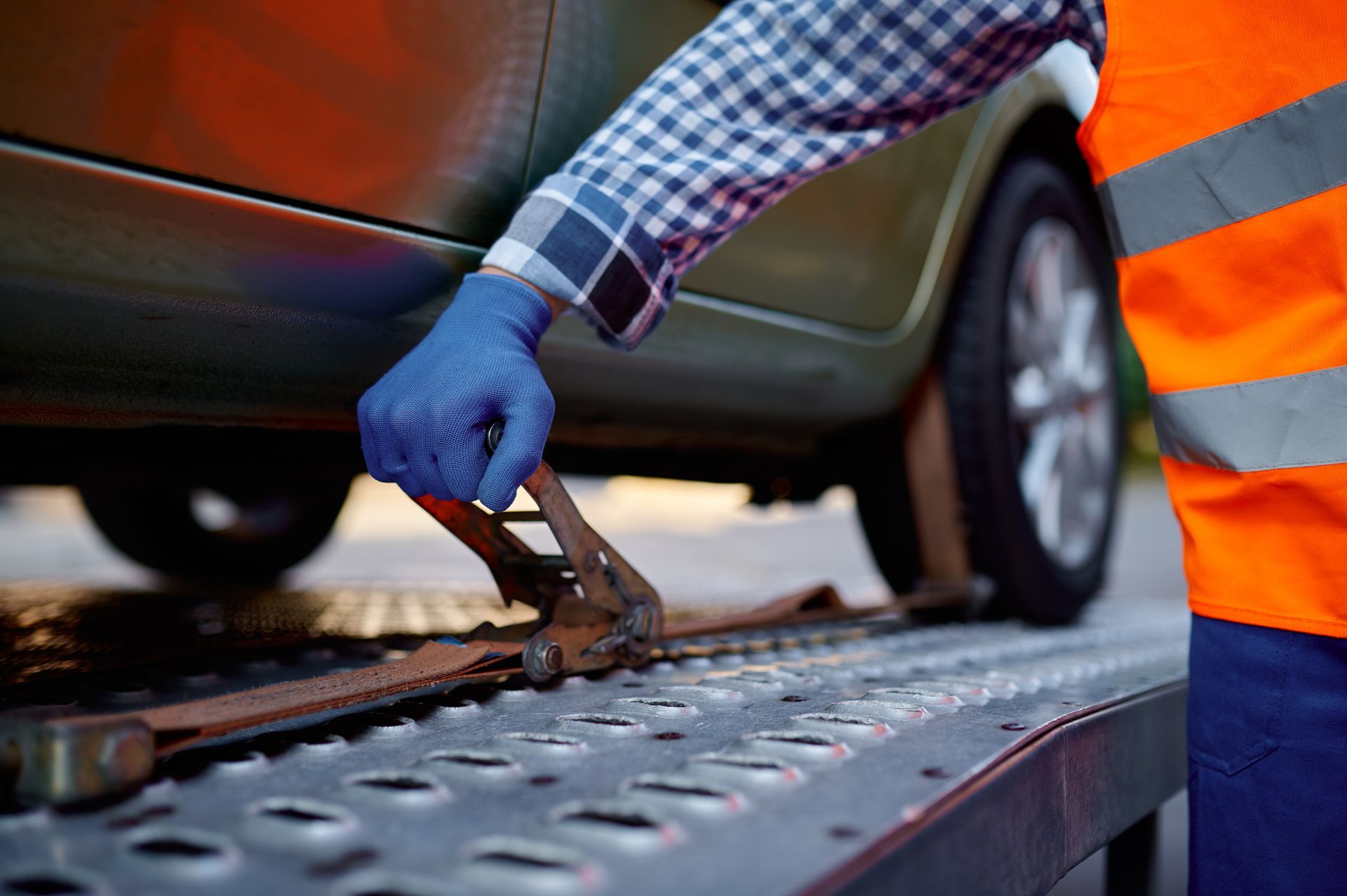 A person in work gloves secures a car to a tow truck bed with straps