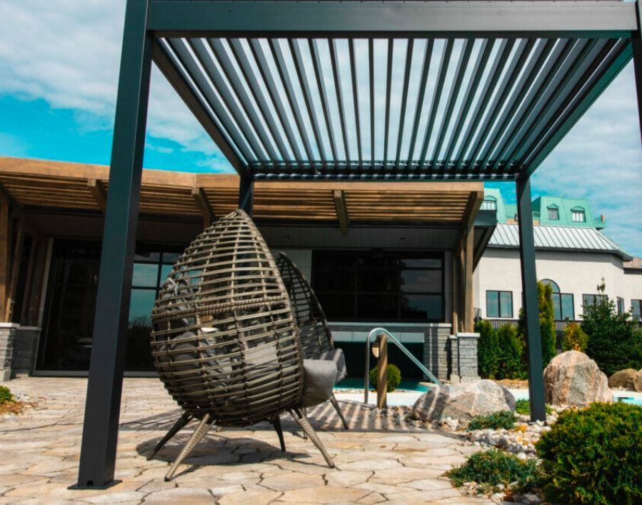 Une chaise en osier est assise sous une pergola devant une maison.