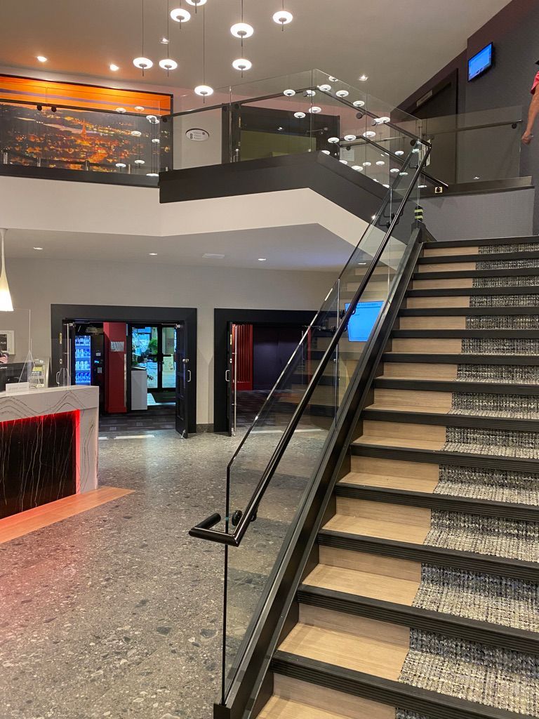 Un hall d'hôtel avec des escaliers menant au deuxième étage et une balustrade en verre.