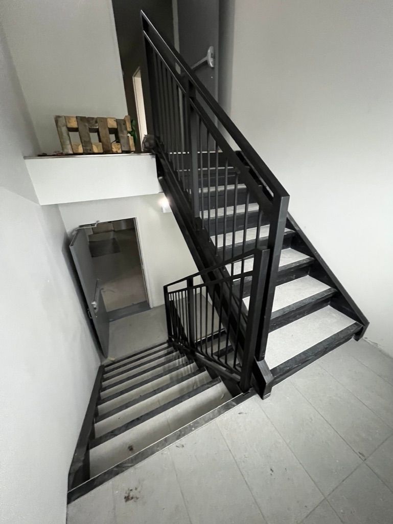 Un escalier avec une rampe noire menant au deuxième étage d'un immeuble.