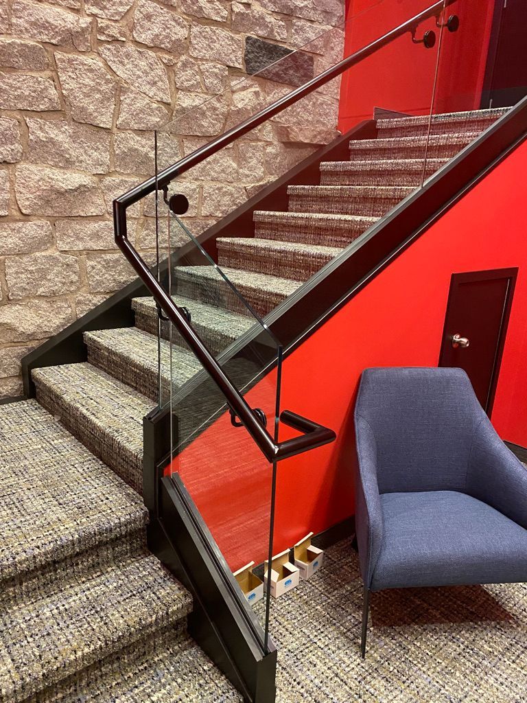 Un escalier avec une rampe en verre et une chaise à côté.