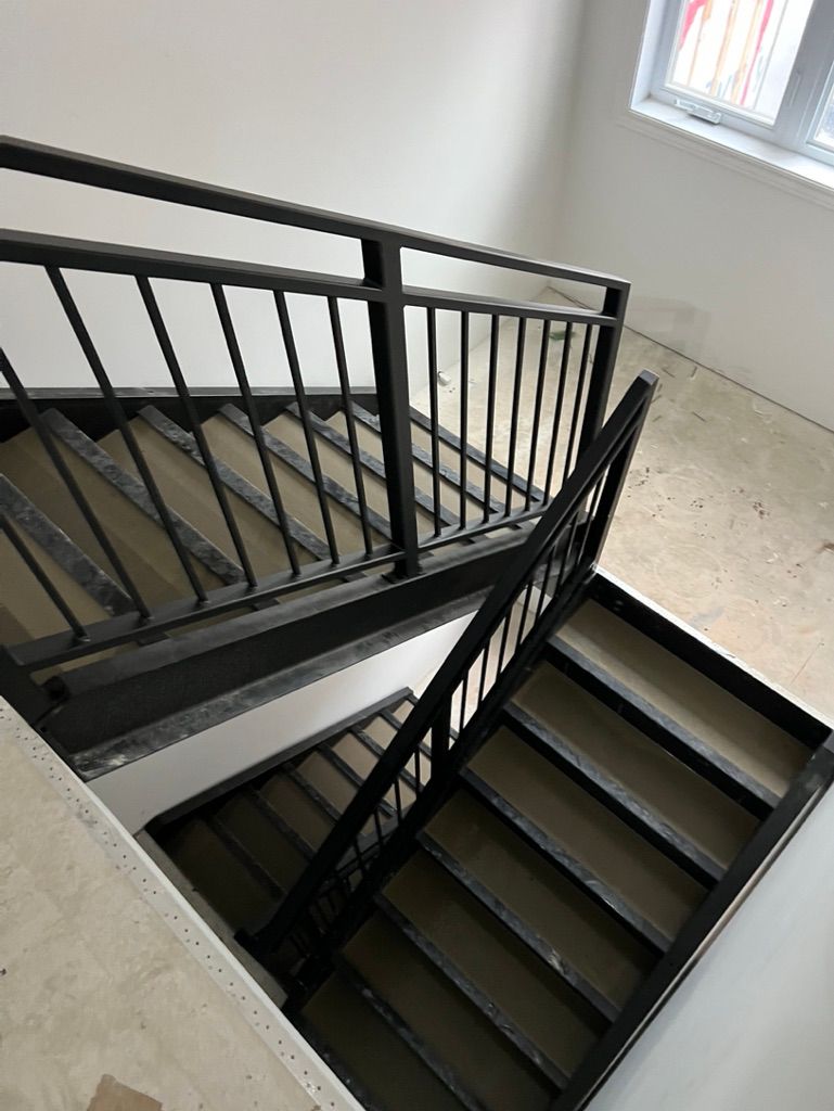 Un escalier avec une rampe noire monte et descend dans une pièce.