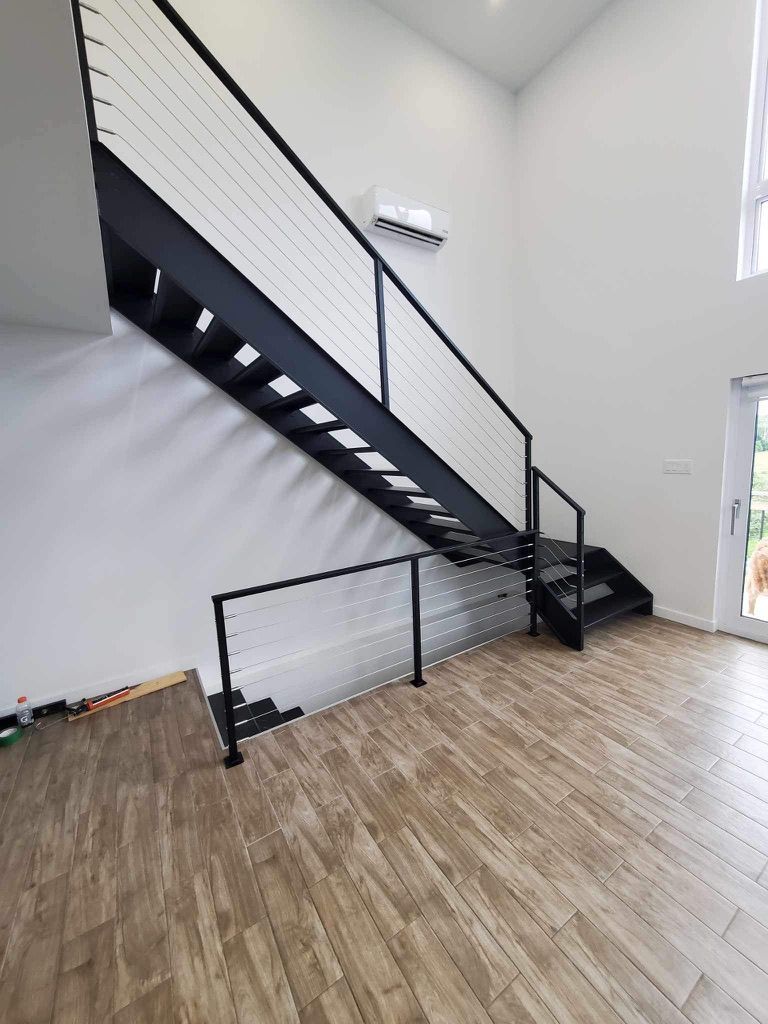 Un escalier noir avec une rampe blanche se trouve dans une pièce avec un plancher en bois.