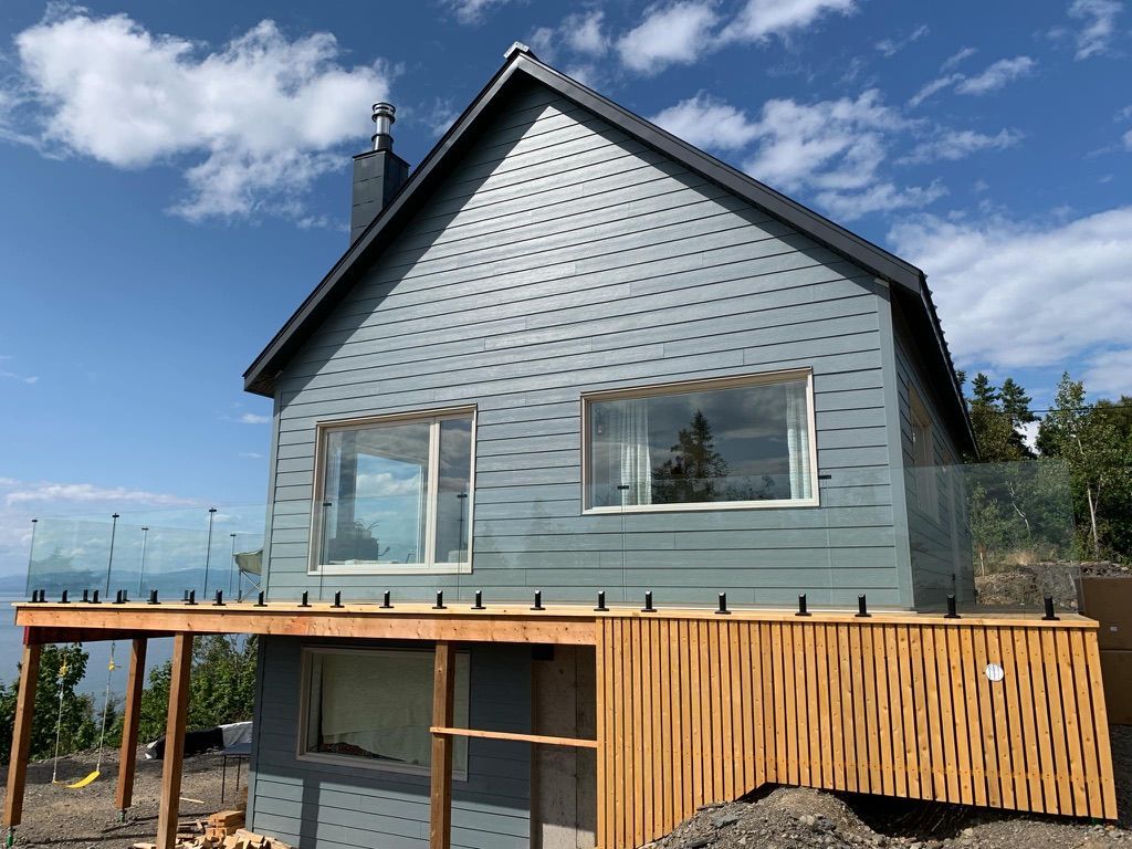 Une grande maison avec une terrasse en bois et une balustrade en verre.