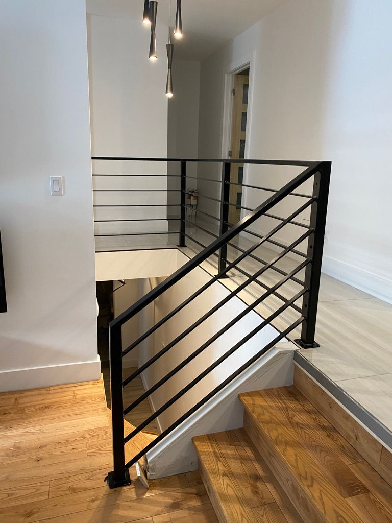 Un escalier avec une rampe noire et des marches en bois dans une maison.