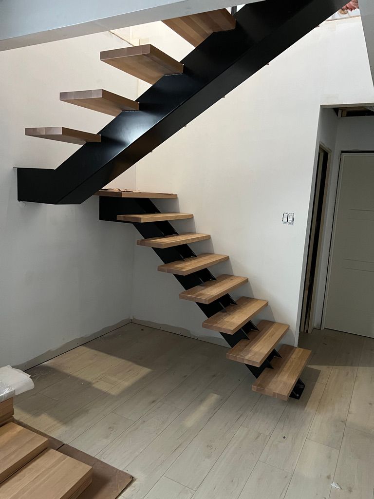 Un escalier noir avec des marches en bois se trouve dans une pièce.