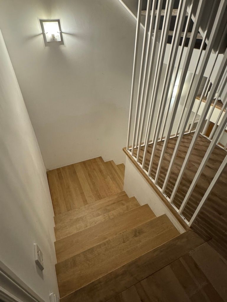 Un escalier en bois avec une rampe blanche et une lumière sur le mur.