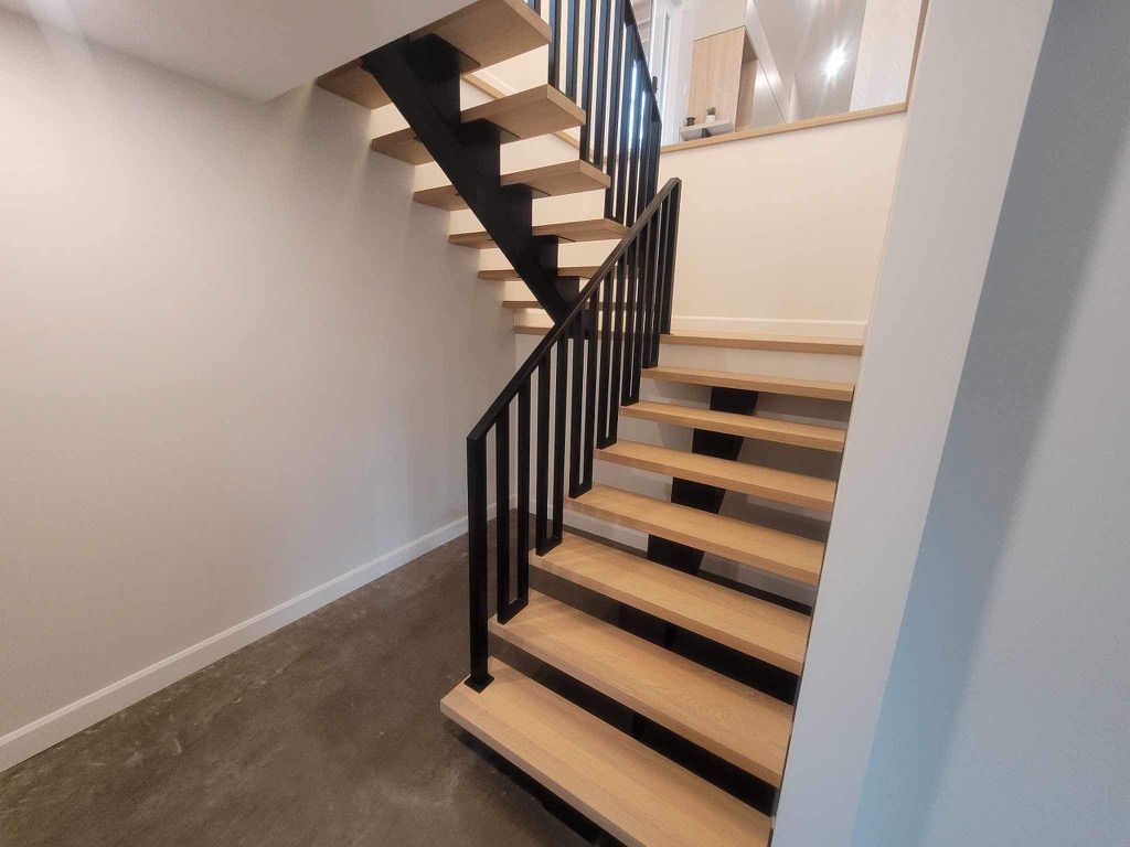 Un escalier en bois avec une rampe noire dans un couloir.
