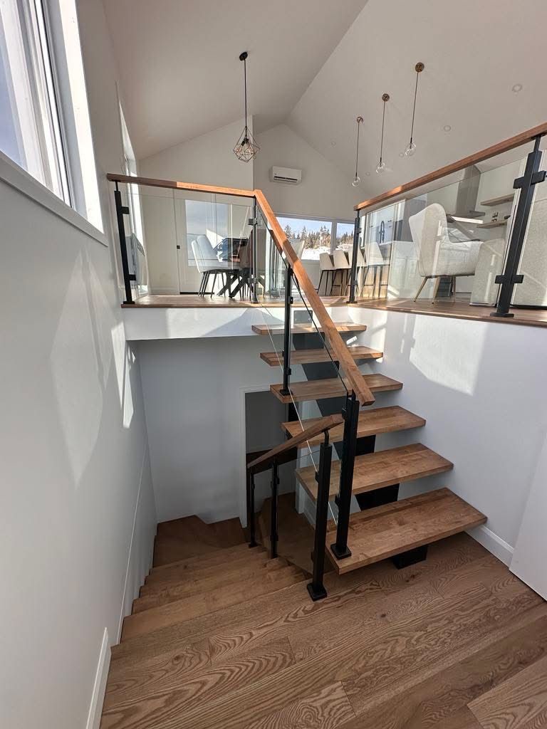 Un escalier en bois avec une rampe en verre menant au deuxième étage d'une maison.