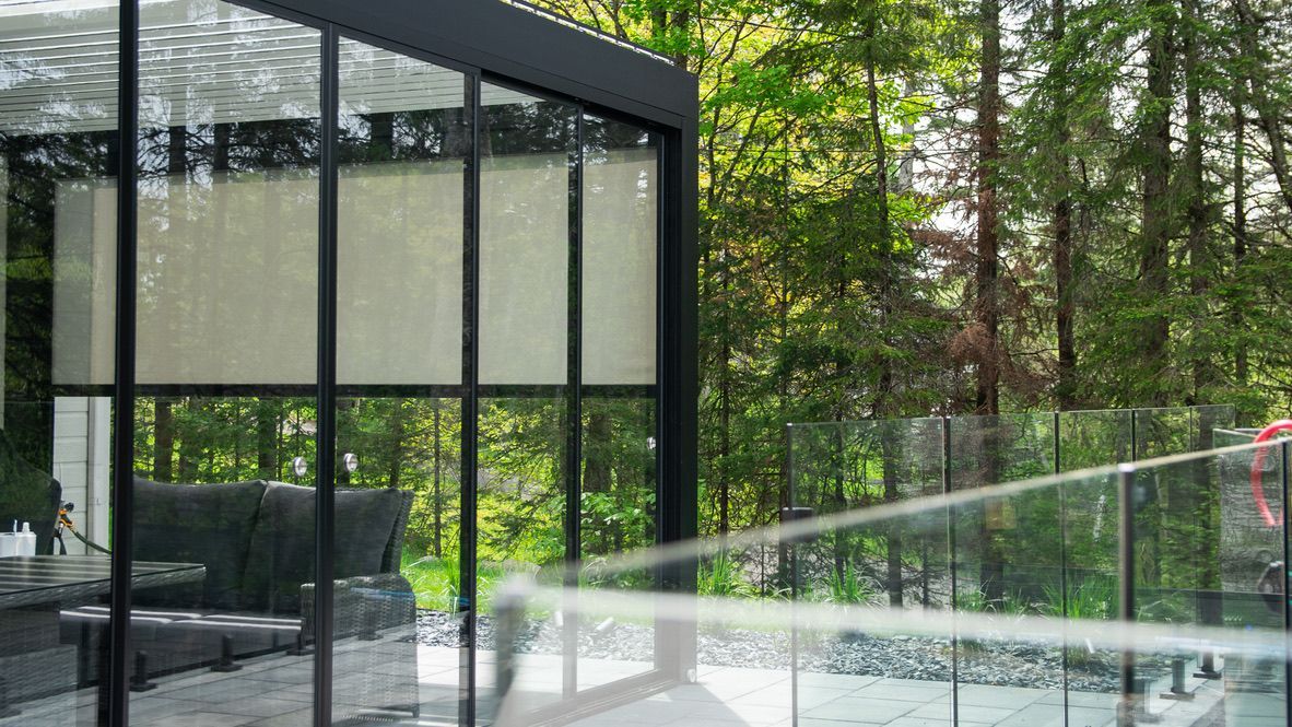 Un patio avec une pergola et une balustrade en verre entouré d'arbres.