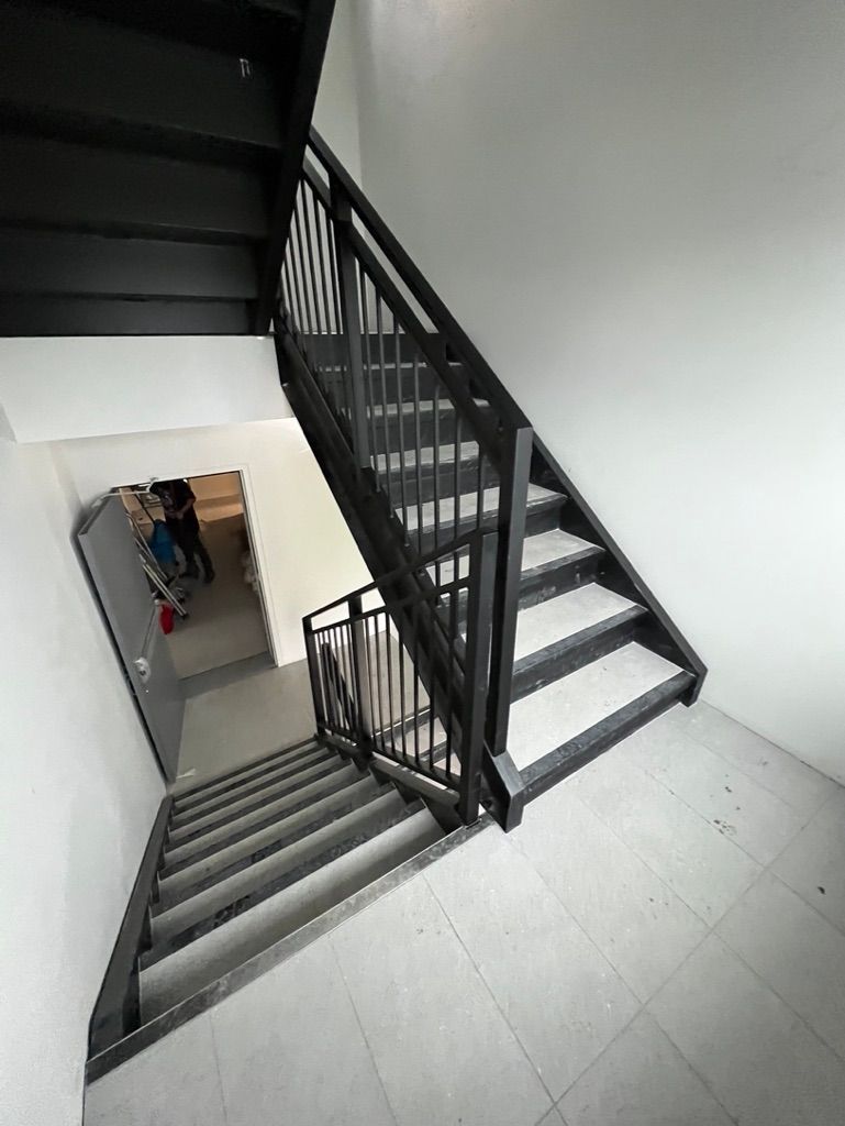 Un escalier noir avec une rampe en métal menant au deuxième étage d'un immeuble.