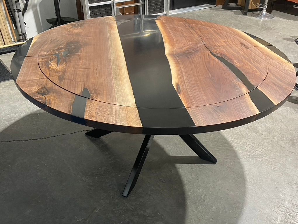 Une table ronde en bois avec une base noire est posée sur un sol en béton.