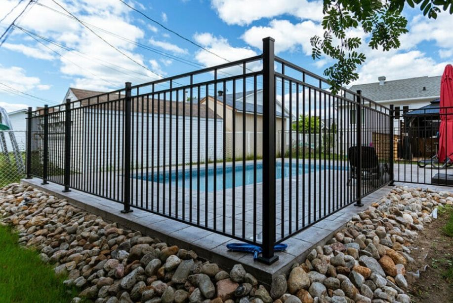 Une clôture en métal noir entoure une piscine dans une cour arrière.