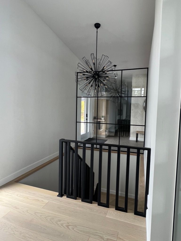 Un escalier avec une rampe noire et un lustre suspendu au plafond.