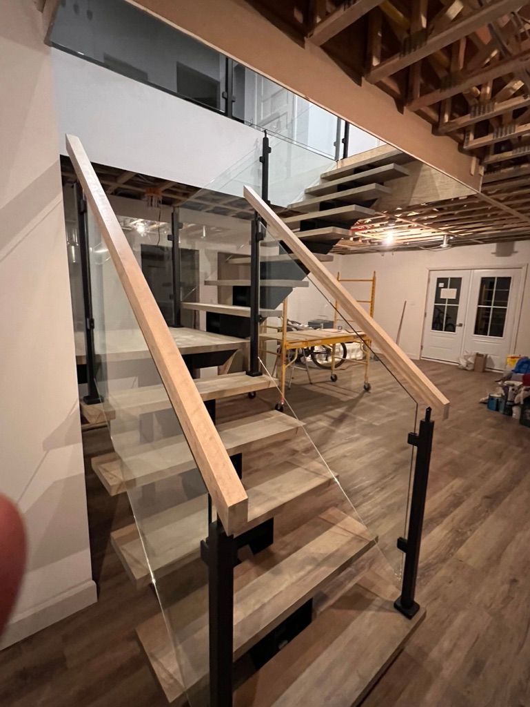 Un escalier en bois avec une rampe en verre est en cours de construction dans une maison.