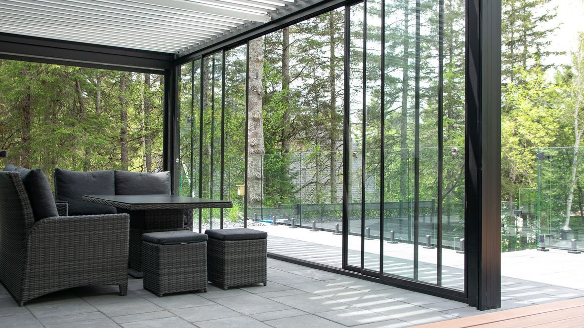 Un patio avec un canapé, une table, des chaises et des poufs dans une pièce avec des portes coulissantes en verre.