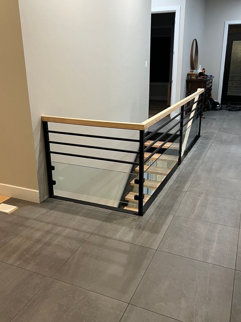 Un escalier avec une rampe en verre et une main courante en bois dans un couloir.