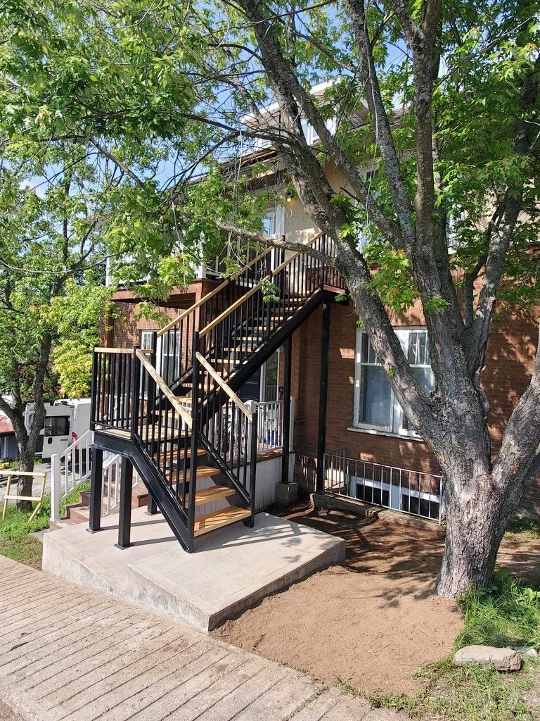 Une maison avec des escaliers menant à une terrasse et un arbre devant.